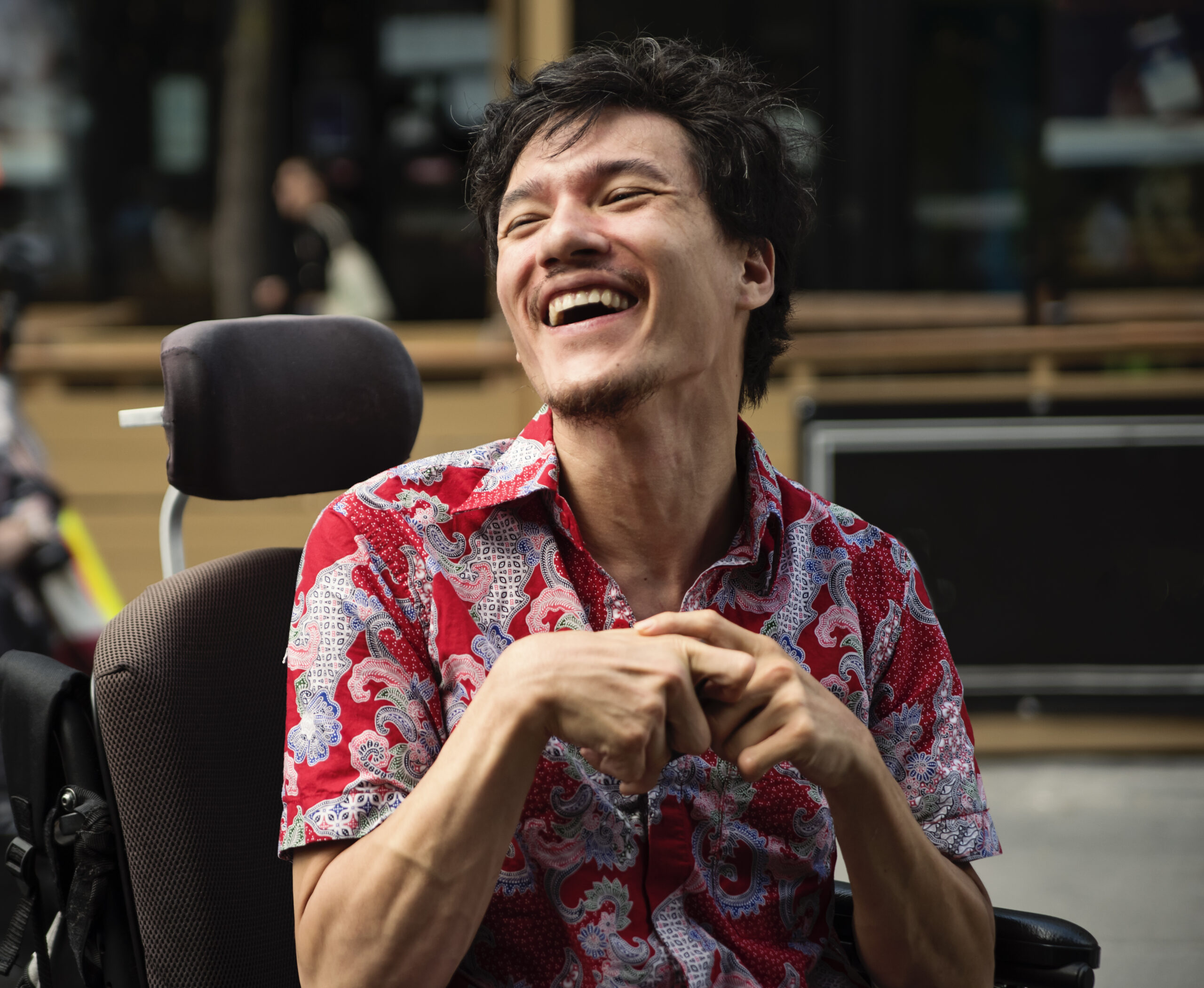 Young man with cerebral palsy laughing outdoors in city.