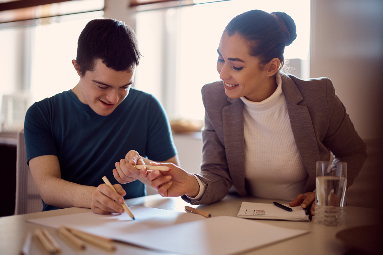 Young happy down syndrome man having special education class with his psychologist at home.